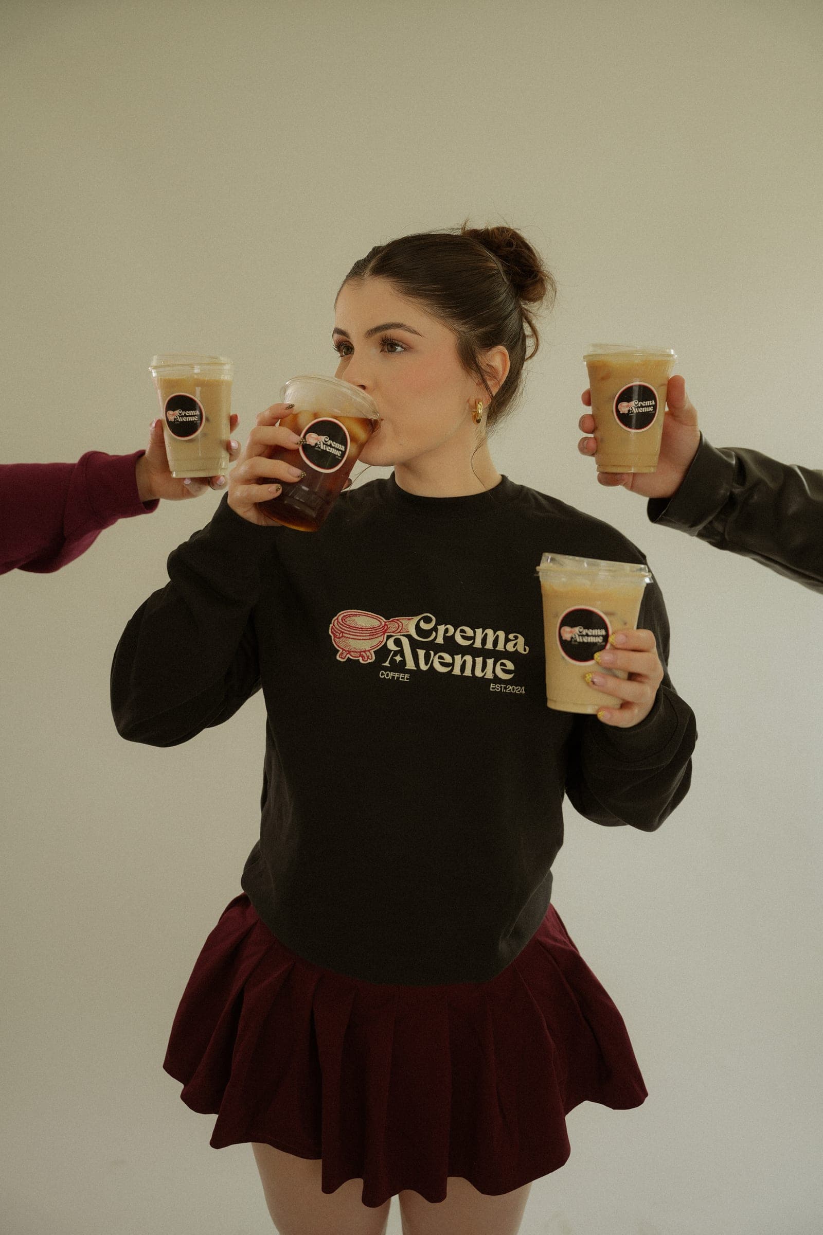 Brianna raising a Crema Avenue iced coffee with three more in the frame